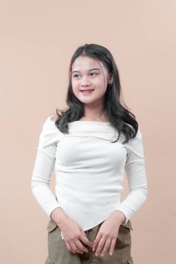 Uzun kollu beyaz bluzlu Asyalı bir kadın nazikçe gülümseyerek, özgüvenini, zarafetini ve doğal güzelliğini modern bir portrede ifade ediyor..