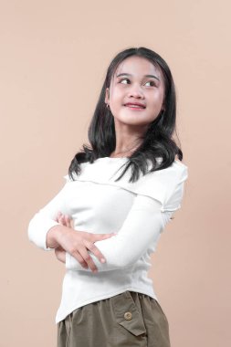 Uzun kollu beyaz bluzlu Asyalı bir kadın kollarını kavuşturup neşeli bir gülümsemeyle yukarı bakıyor. Reklam amaçlı modern bir hayat tarzı portresi için iyimserlik, güven ve zarafet ifade ediyor..