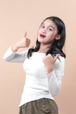 Neşeli, genç Asyalı bir kadın, parlak bir ifadeyle gülümsüyor, günlük beyaz kıyafetiyle, pozitifliği, onayı ve başarıyı sembolize eden bir jest yapıyor..