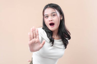 Şaşırmış bir ifadeyle elini kaldıran genç bir Asyalı kadın. Sıradan beyaz kıyafetler giymiş. Uyarı, reddetme, koruma ve ihtiyatı sembolize ediyor..