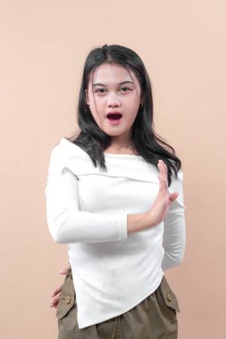 Şaşırmış yüz ifadesine sahip genç Asyalı bir kadın dur işareti yapıyor. Günlük beyaz gömlek giyiyor. Reddetmeyi, uyarıyı, duyguyu ve iletişimi simgeliyor..