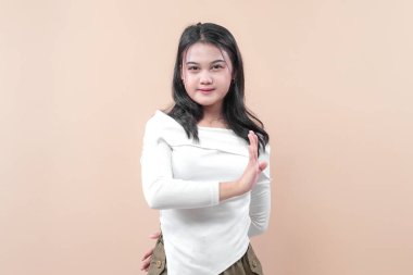 Beyaz bluzlu, kendine güvenen genç Asyalı kadın sakin bir ifadeyle el hareketini durduruyor. Reddi, uyarıyı, farkındalığı, iletişimi ve profesyonelliği simgeliyor..