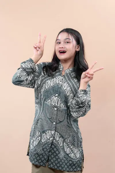 Geleneksel Batik kıyafetler giyen Asyalı bir kadın iki eliyle barış işareti gösterirken, yaratıcı reklamcılık ve ticari kullanım için uygun neşe, güven ve kültürel gurur ifade ediyor..