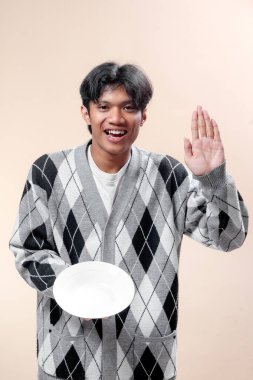 Beyaz bir tabak tutarken gülümseyen ve elini kaldıran neşeli Asyalı bir adam selamlamayı, arkadaşlığı ve pozitif yaşam tarzını sembolize ediyor..