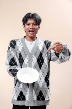 Gri baklava desenli süveter giyen neşeli Asyalı bir adam beyaz bir tabağa bakarken gülümsüyor. Reklamcılığa uygun güven, pozitiflik ve yaşam tarzı kavramları gösteriyor..