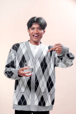 Bir bardak su tutarken gülümseyen ve onu işaret eden gri baklava desenli Asyalı adam, sağlığı, tazeliği, pozitifliği ve kendine güvenen bir yaşam tarzını simgeliyor..