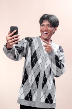 Asyalı adam akıllı telefonu tutarken ve parmak hareketi yaparken gülümsüyor, neşeli enerji, güven ve modern yaşam tarzı gösteriyor, reklam, iş ve teknoloji temaları için mükemmel..