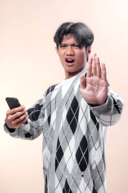 Asyalı adam şaşırmış bir ifadeyle akıllı telefonu tutuyor, dur hareketi olarak elini kaldırıyor, reddedilmeyi, uyarıyı, iletişimi, modern yaşam tarzını ve iş konseptini sembolize ediyor.