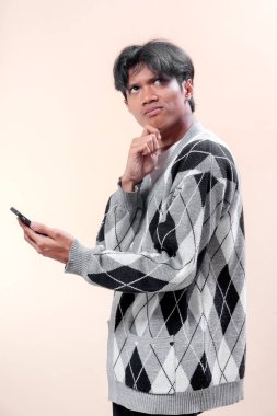 Asyalı adam akıllı telefonu düşünceli bir ifadeyle tutuyor, sanki karar veriyormuş gibi çeneye dokunuyor, odaklanma, iş planlama, modern yaşam tarzı, iletişim ve profesyonel konsepti sembolize ediyor..