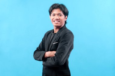 Siyah takım elbiseli kendine güvenen genç bir adam, mavi arka planda liderlik, kariyer gelişimi ve modern profesyonelliği simgeleyen parlak bir gülümseme ile poz veriyor..