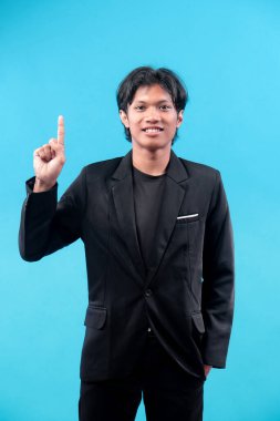 Siyah takım elbiseli genç adam mavi arka planda bir parmağını kaldırırken özgüvenle gülümsüyor, fikri, başarıyı, liderliği, ilgiyi, motivasyonu ve profesyonel tutumu simgeliyor..
