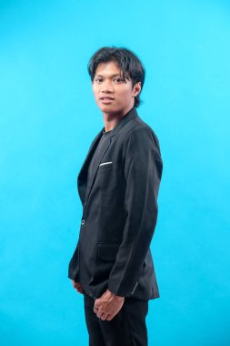 Siyah takım elbiseli genç Asyalı bir adam, sakin bir ifadeyle, zarafeti, profesyonelliği ve modern tarzı yansıtan, kendinden emin bir şekilde öne bakıyor..