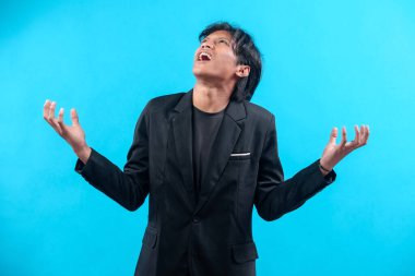 Siyah takım elbiseli genç bir Asyalı ağzı açık yukarı bakar ve ellerini kaldırır. Öfke ve hayal kırıklığını gösterir. Stres, duygu ve dramatik ifadeyi temsil eder..