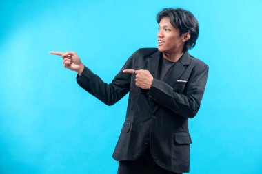 Siyah takım elbiseli ve tişörtlü genç bir adam gülümseyerek, özgüven, olumlu tavır ve mavi arka planda profesyonel karizmayı gösterirken iki elini de kenarda gezdiriyor..