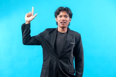 Siyah takım elbiseli ve tişörtlü genç bir adam bir elini kaldırır ve işaret parmağıyla fikrini, özgüvenini ve mesleki tutumunu açık mavi bir arkaplanda gösterir..