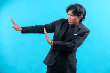 Siyah takım elbiseli genç bir adam ciddi bir yüzle kollarını yana doğru uzatıyor. Dikkat, reddedilme ve profesyonel tavır sergileyen bir savunma hareketi sergiliyor..