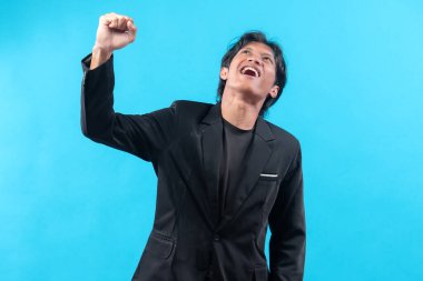 Siyah takım elbiseli neşeli genç bir adam heyecan içinde yumruğunu kaldırırken ışıl ışıl gülümserken güven, hırs, liderlik ve iş ve kariyer kavramlarındaki profesyonel başarıyı sembolize ediyor..
