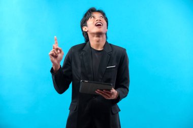 Siyah takım elbiseli genç bir adam elinde tabletle yukarı doğru tuhaf bir ifadeyle, modern iş fikirlerini ve profesyonel yaratıcılığı temsil ediyor..