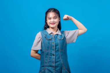 Kolunu kaldırmış kaslarını gösterirken gülümseyen kendinden emin genç Asyalı kadın. Yüz ifadesi ve duruşu güç, güç, başarı ve kendine güven verir..