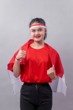 Kırmızı ve beyaz kıyafetli neşeli genç bir kadın gururla gülümserken, iyimserliği, vatanseverliği ve Endonezya Bağımsızlık Günü 'nün coşkulu ruhunu simgeleyen bir jest gösteriyor..