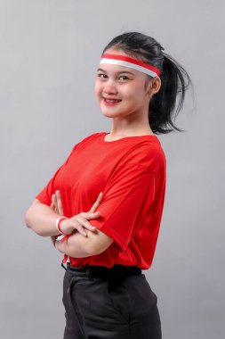 Kırmızı-beyaz saç bandı ve kurdeleli kendine güvenen genç kadın gülümseyerek Endonezya Bağımsızlık Günü 'nün ruhunu sembolize ediyor..