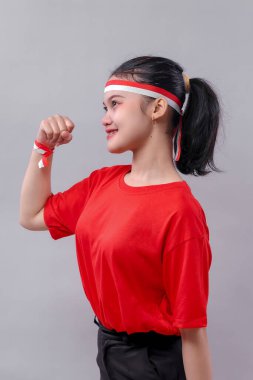 Endonezyalı genç bir kadının yakın plan görüntüsü. Yumruğunu sıkmış gururla gülümsüyor. Kırmızı ve beyaz aksesuarlar takıyor ve bağımsızlık ve birlik ruhunu kutluyor..