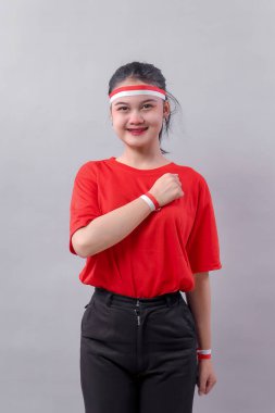 Kırmızı ve beyaz bileklik ve saç bandı takan Endonezyalı genç kadın gururla yumruğunu göğsüne koyar. Bağımsızlık Günü kutlamalarının milliyetçiliğini, birliğini ve neşesini ifade eder..