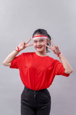 Kırmızı kıyafetli neşeli Endonezyalı kadın, Endonezya Bağımsızlık Günü 'nü kutlamak için kırmızı-beyaz saç bandı ve bileziklerle gururla gülümsüyor..