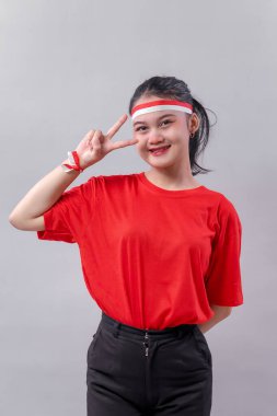 Endonezya 'nın Bağımsızlık Günü' nü gururla anmak için kırmızı-beyaz aksesuarlar takan kırmızı tişörtlü ve siyah pantolonlu genç Endonezyalı bir kadın zafer jesti ile gülümsüyor..