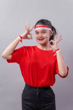 Kırmızılı mutlu Endonezyalı kadın çift tamam işareti gösteriyor, neşeyle gülümsüyor. Bağımsızlık Günü kutlaması ruhu için kırmızı-beyaz aksesuarlar giyiyorlar..