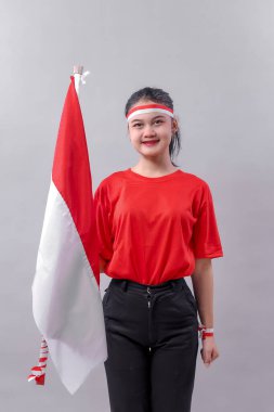 Endonezyalı genç bir kadın kırmızı ve siyah giyinmiş, kırmızı ve beyaz bayrak tutarken gülümsüyor. Gururlu ifade vatanseverlik ve bağımsızlık kutlaması ruhunu gösteriyor..