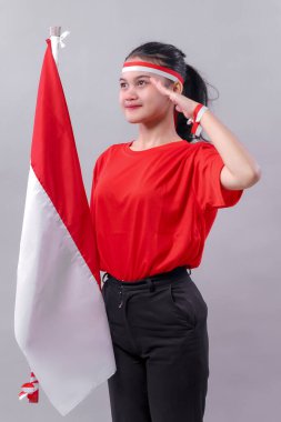 Onurlu Endonezyalı genç bir kadın, Bağımsızlık Günü için kırmızı ve beyaz giyinmiş ulusal bayrağı tutarken kendine güvenen bir gülümsemeyle selamlıyor..