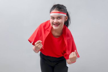 Kırmızı beyaz elbiseli heyecanlı Endonezyalı kız neşeli bir zafer pozu veriyor. Kendine güvenen bir gülümsemeyle Bağımsızlık Günü 'nü tutkuyla ve gururla kutluyor..