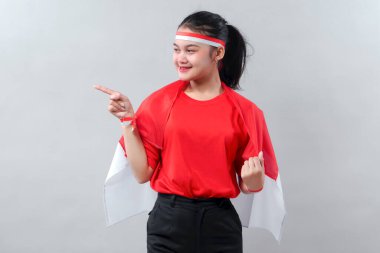 Kırmızı ve beyaz giyen neşeli genç bir kadın Endonezya Bağımsızlık Günü 'nü gururla kutluyor, neşe ve güvenle işaret ediyor..