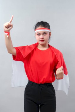 Kırmızı gömlekli ve bantlı kendine güvenen Endonezyalı genç bir kadın parmağını yukarı kaldırıyor, kırmızı ve beyaz bayrağa sarılı, birlik, gurur ve vatanseverliği simgeliyor..