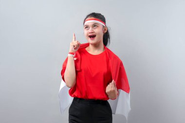 Bağımsızlık Günü 'nde kırmızı ve beyaz kıyafet giyerken işaret parmağını kaldıran parlak fikir ifadeli mutlu Endonezyalı genç kadın..