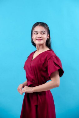 Şık kırmızı elbiseli genç Asyalı kadın zarif, kendine güvenen ve doğal çekiciliğini ifade ederken nazikçe gülümsüyor. Yaşam tarzı, iş hayatı ve reklam kavramları için mükemmel..