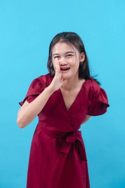 Kırmızı elbiseli genç bir kadın, elini ağzının yanında tutarken gülümsüyor, sanki fısıldıyor ya da bağırıyor gibi..