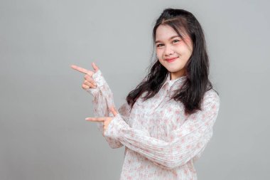 Asyalı genç bir kadın iki eliyle yan tutarak gülümserken neşeli ve davetkar bir ifade sergiliyor. Promosyon reklamları, sunumlar veya pazarlama kavramları için ideal.