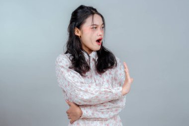 Şok olmuş ve savunmacı yüz ifadesine sahip genç bir Asyalı kadın, reddedilme ya da korku sinyali vermek için elini kaldırıyor, izole stüdyo ortamında güçlü duygular ve sözsüz tepkiler veriyor..