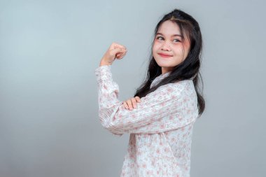 Gülümseyen genç Asyalı kadın kendine güvenen bir duruş sergiliyor. Gururunu, pozitifliğini ve iç gücünü gösteriyor. Onun parlak ifadesi güç ve kararlılığı iletir..