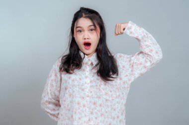 Uzun saçlı genç Asyalı kadın şaşırmış bir yüz ifadesi sergiliyor. Kolunu rahatça esnetiyor. Beklenmedik bir gücü ve duygusal zıtlığı simgeliyor..