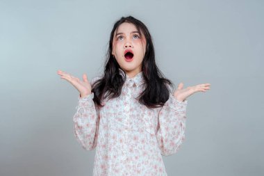 Şaşırmış genç Asyalı kadın ağzı açık ve elleri şokla ya da şaşkınlıkla yukarı bakıyor. Stüdyo portresi anlamlı yüz, duygusal tepki ve dramatik jest gösteriyor..
