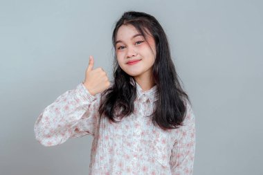 Çekici bir gülümsemesi olan kendine güvenen genç Asyalı kadın olumlu ve onaylı bir jest yapıyor. Çiçekli gömlek ve nötr arkaplan ile yakın çekim stüdyo portresi.