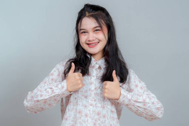 Diş telleri parlak gülümseyen mutlu Asyalı bir kadın. Bu arada iki başparmak havaya kalkıyor. Onaylıyor, tatmin oluyor ve neşeli ve arkadaşça cesaretlendiriyor..