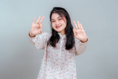 Uzun siyah saçlı, gülümseyen genç Asyalı kadın kameraya doğru çift tamam işareti gösteriyor. Neşeli ve kendinden emin ifadesi onu pozitif reklam temaları için ideal kılıyor..