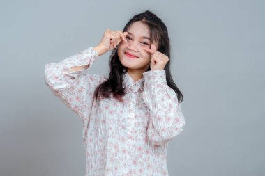 Çekici, genç Asyalı bir kadın tatlı tatlı gülümserken iki eliyle küçük bir kalp hareketi yapıyor, neşeli bir sevgi ve neşeli bir sevinç ifadesi sergiliyor..