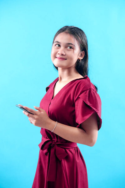 A young woman in a red dress holding a smartphone and looking up with a thoughtful smile, representing confidence, creativity, modern lifestyle, and professional concept.