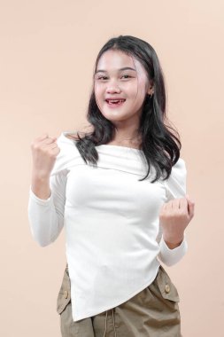 Mutluluktan gülümseyen ve yumruklarını kaldıran Asyalı bir kadın, güven, başarı ve iş hayatı ve temaları için pozitif enerjiyi simgeliyor..