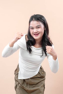 Asyalı bir kadın kendine güvenen yumruklarıyla gülümser, enerji ve kararlılık gösterir, motivasyon, güç ve başarıyı temsil eder, yaşam tarzı ve iş kavramları için mükemmeldir..